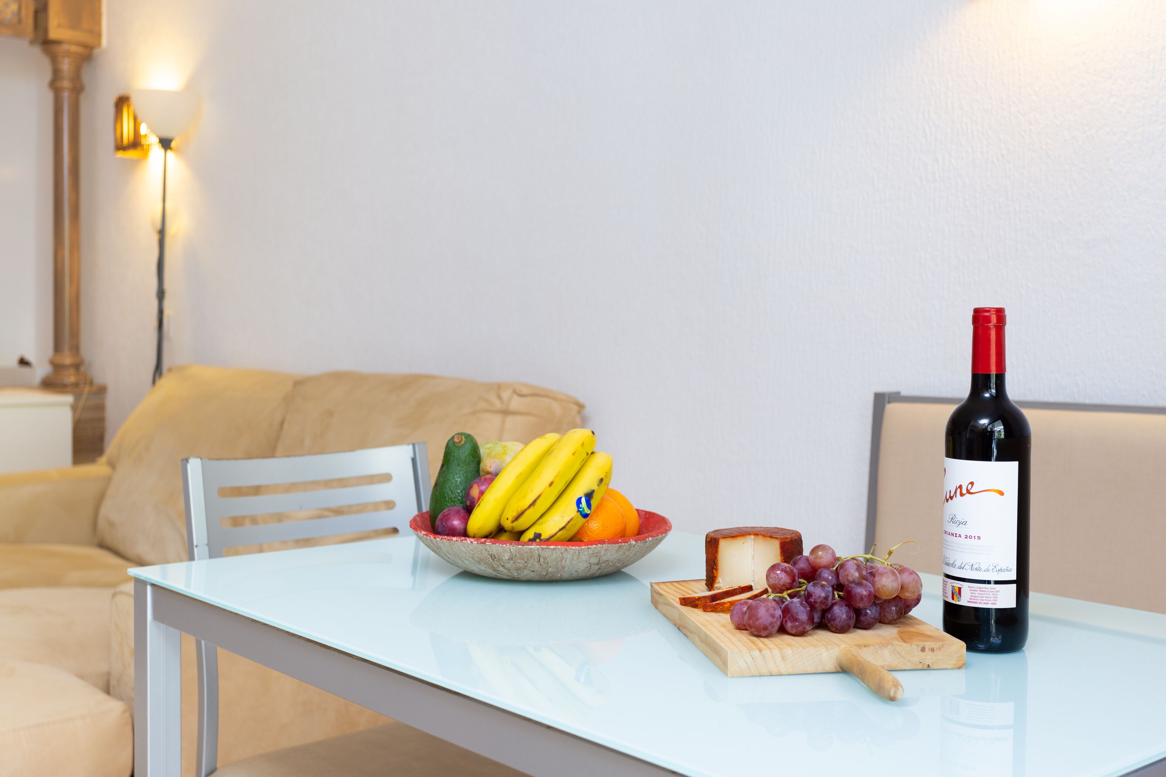 Una mesa de comedor con un bol de fruta, una botella de vino y una tabla de quesos.