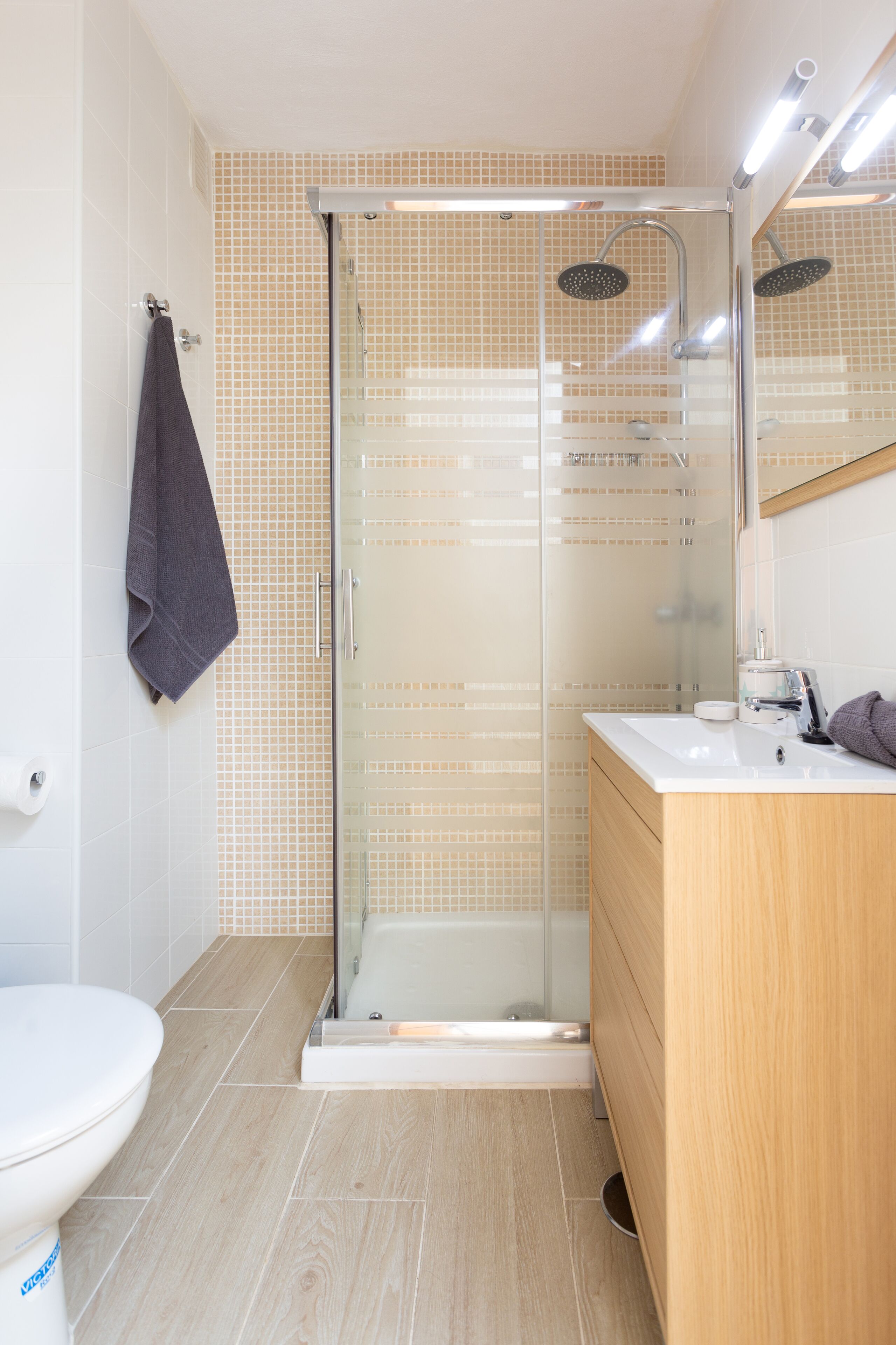 Un bagno moderno con doccia vetrata, water bianco e mobile bagno in legno con specchio.