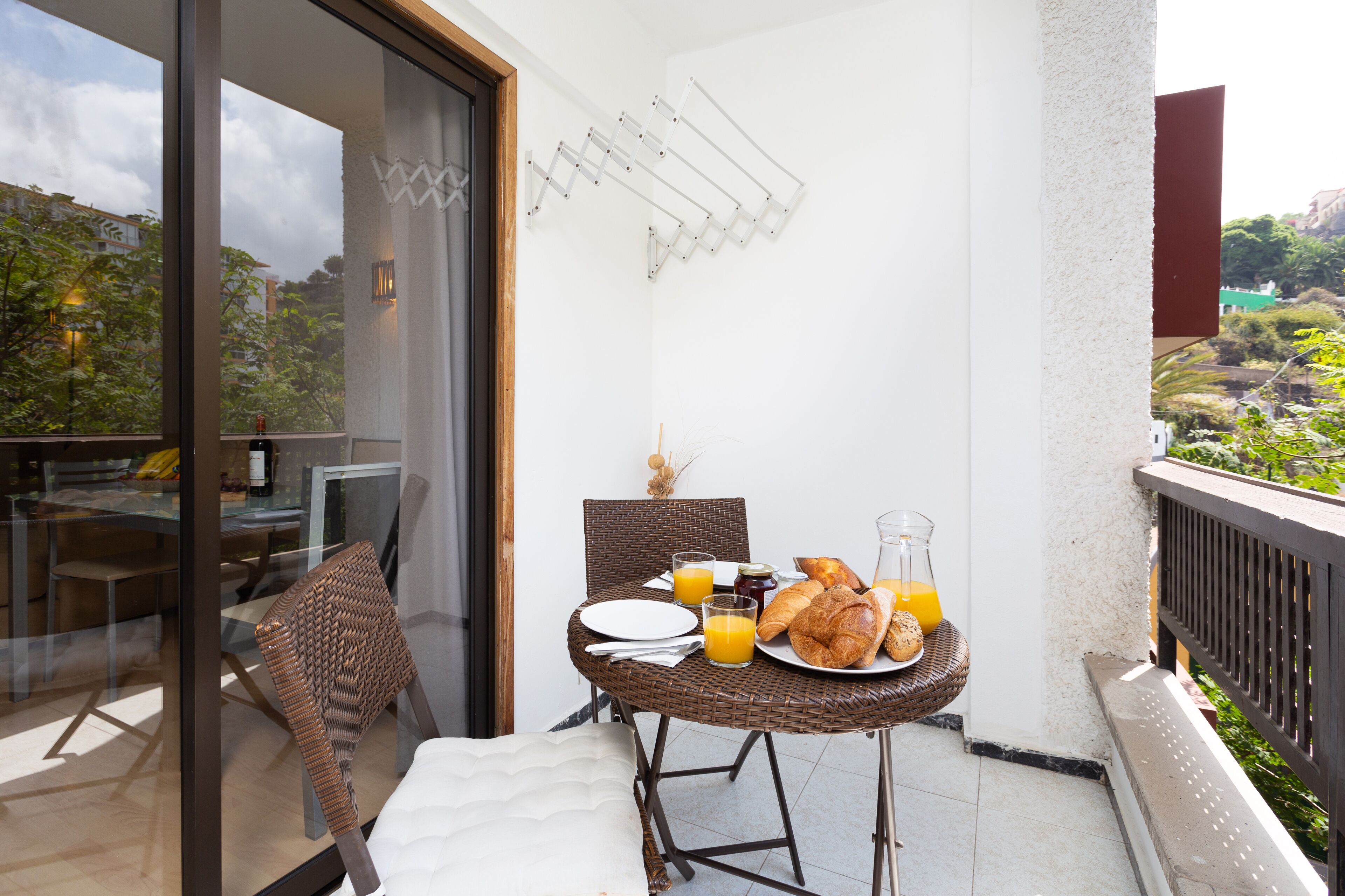 A balcony with a dining table set for breakfast, including croissants, juice, and a glass of orange juice.