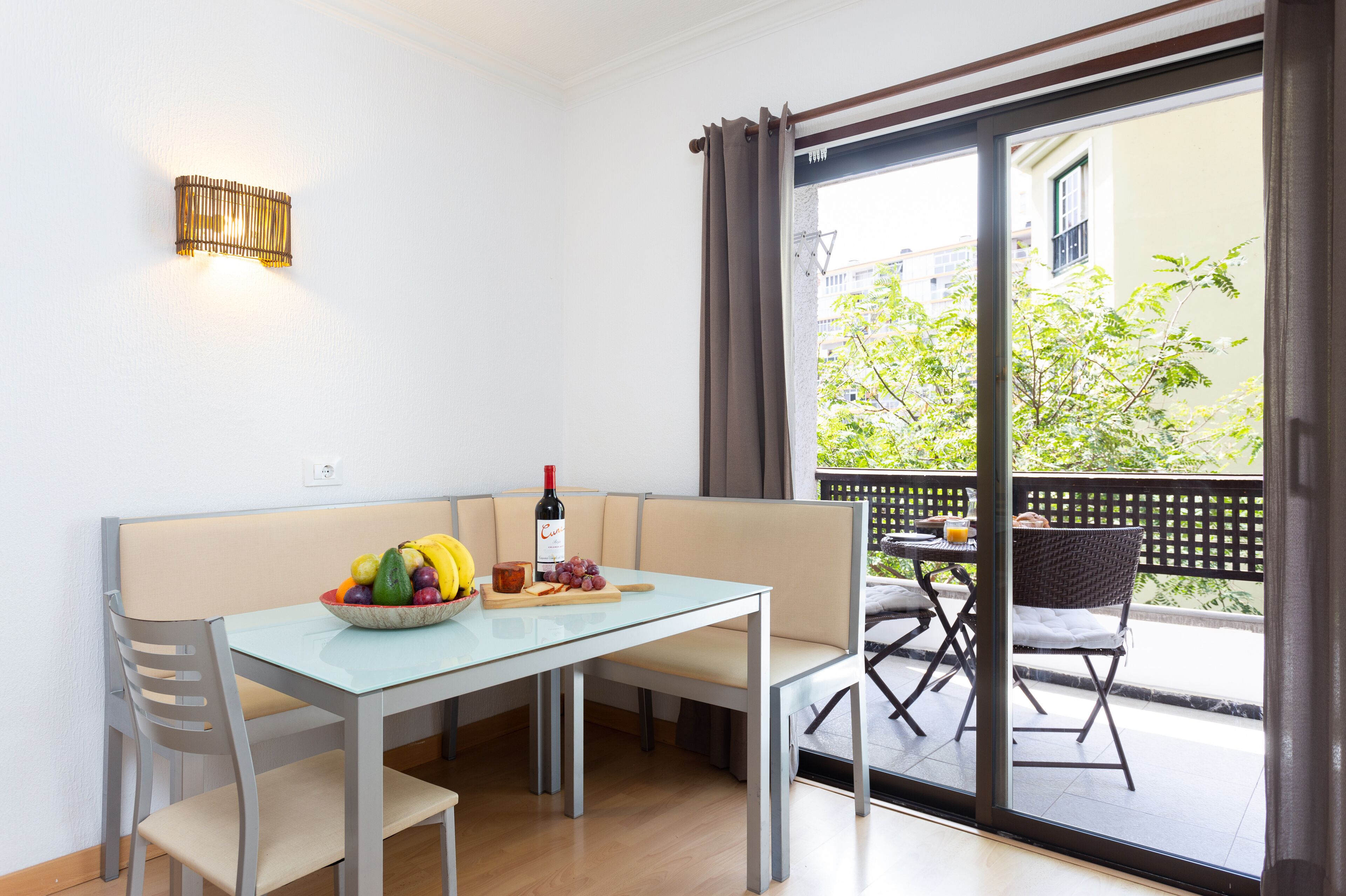 A dining area with a table, chairs, a bowl of fruit, and a bottle of wine.