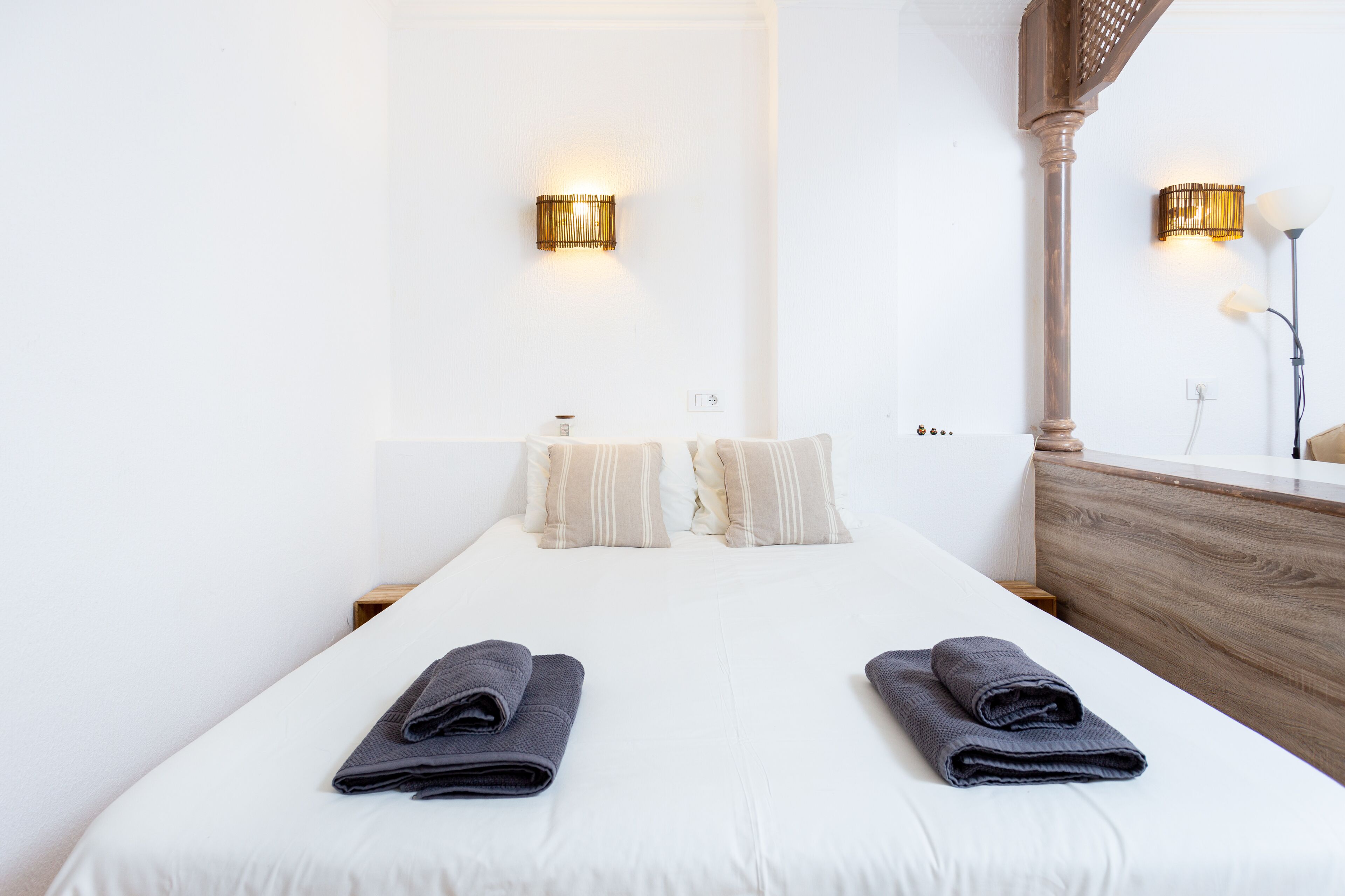 Habitación de hotel con una cama grande, dos lámparas fijadas a la pared, un cabecero de madera y una mesita de noche pequeña.