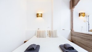 Habitación de hotel con una cama grande, dos lámparas fijadas a la pared, un cabecero de madera y una mesita de noche pequeña.
