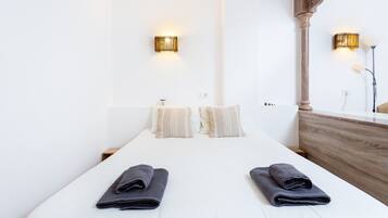 Habitación de hotel con una cama grande, dos lámparas fijadas a la pared, un cabecero de madera y una mesita de noche pequeña.