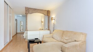 Una sala de estar moderna con un sofá color beige, una mesita negra pequeña y una consola blanca. Se aprecia una viga de techo de madera y dos luces fijadas a la pared.