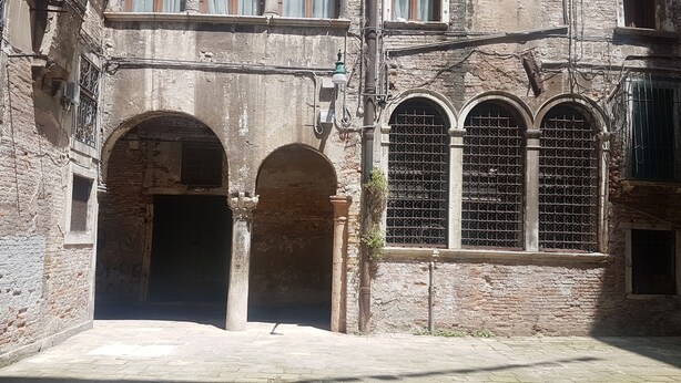 A historic building with arched doorways and a large window with metal bars. - Corte Sconta Mini Loft (Venice)