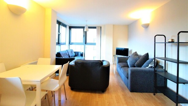 A modern living room with a white dining table, black sofa, and a TV on a stand. - City Walk (Leeds)