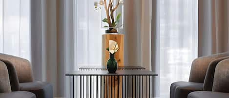 A modern interior with a black metal table, two upholstered chairs, and a vase with white flowers.