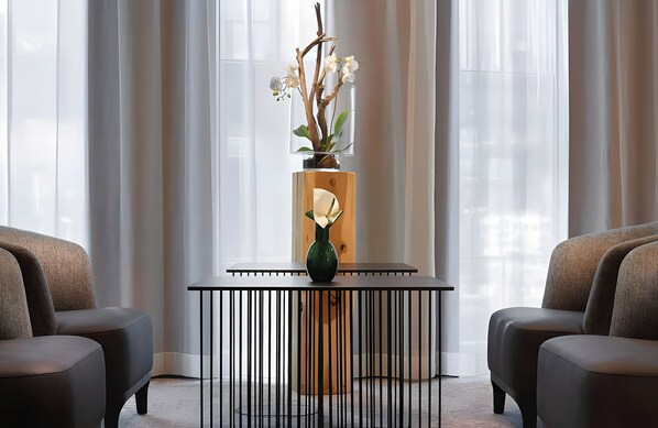 A modern interior with a black metal table, two upholstered chairs, and a vase with white flowers.
