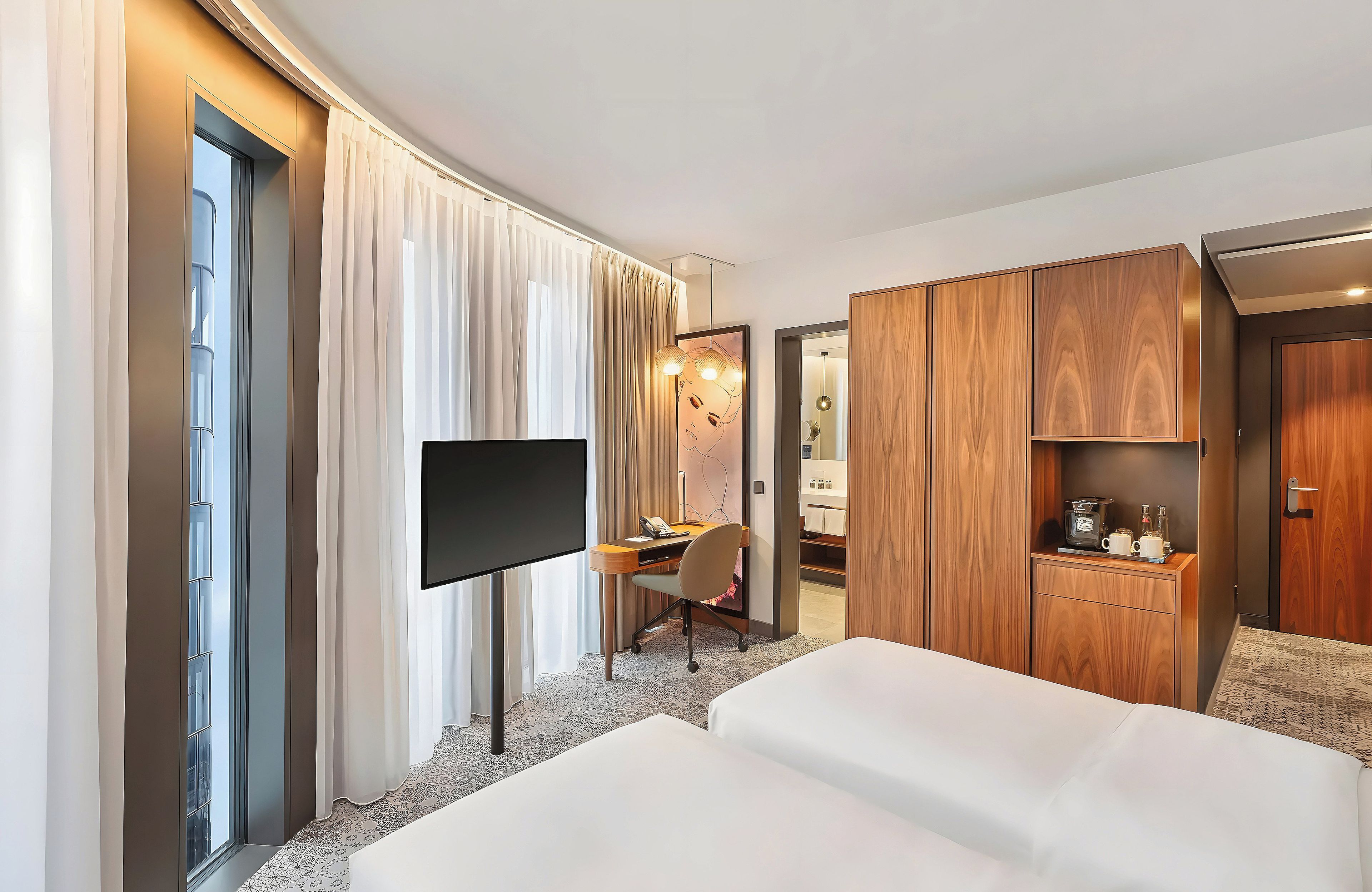 Quarto de hotel com cama, escrivaninha com cadeira, televisão e armário.