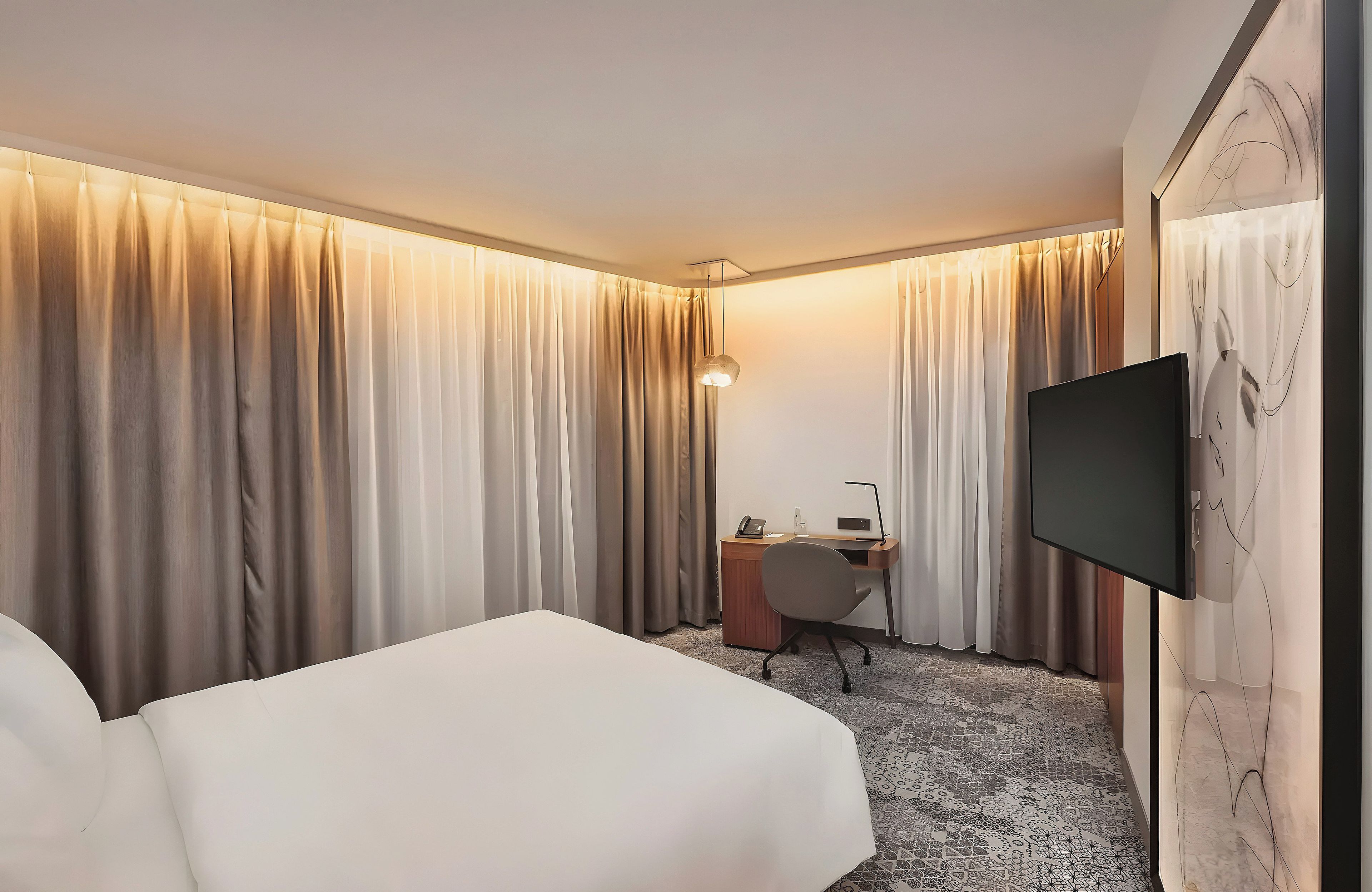 Une chambre d’hôtel avec un lit, un bureau et une chaise, une télévision et des rideaux.