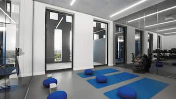 A modern gym with exercise mats, a punching bag, and a view of the city through large windows.