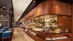 A modern breakfast bar with a curved wooden design, a variety of food items, and neatly arranged plates and glasses. - HYPERION Hotel München (Munich)