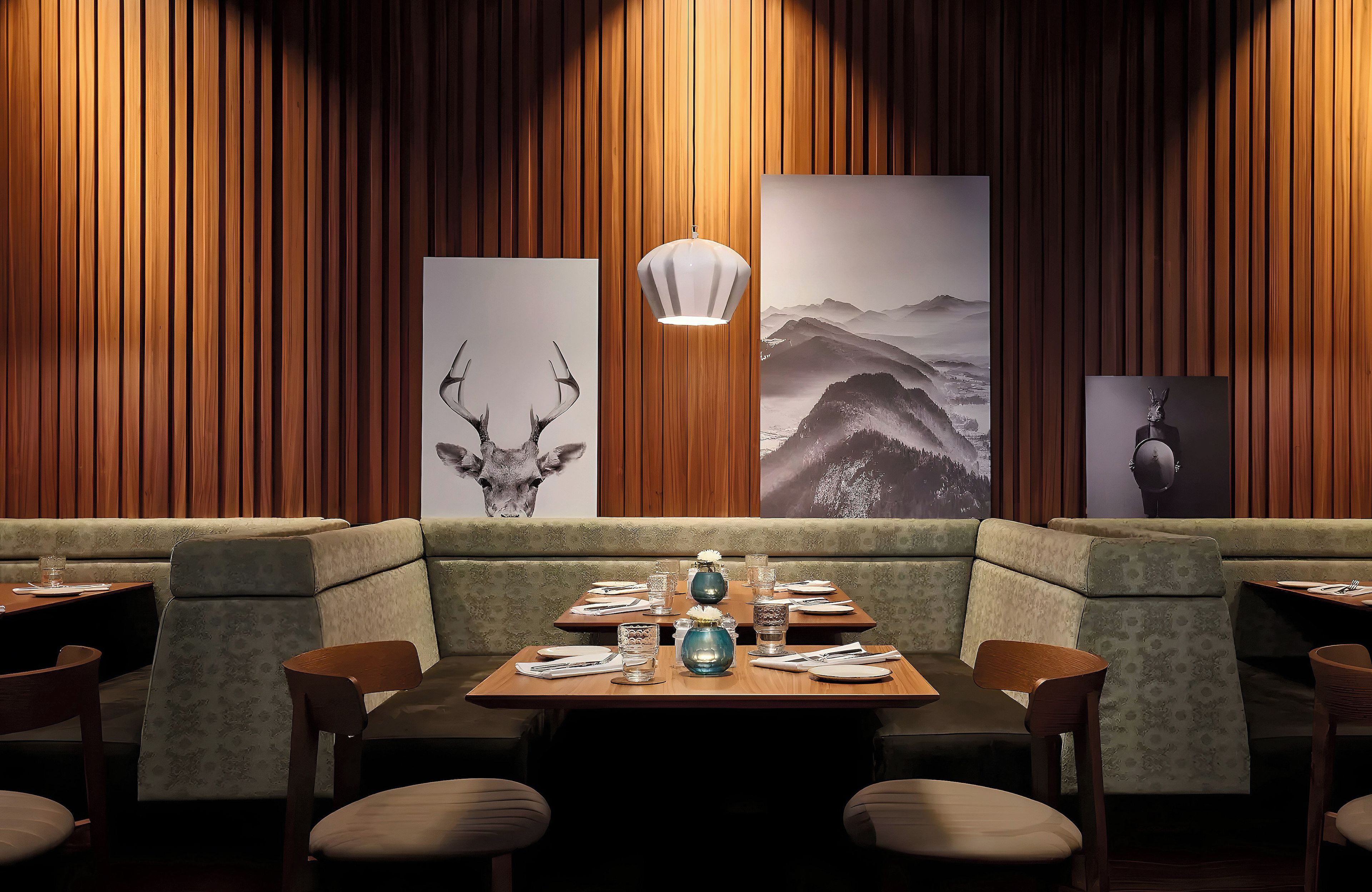 Ein Restaurantinneres mit Holzwandverkleidung, einem zentral platzierten Esstisch für zwei Personen und einem großen Gemälde einer Berglandschaft.