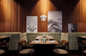 A restaurant interior with wooden panel walls, a central dining table set for two, and a large painting of a mountain landscape.