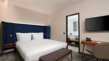 A hotel room with a bed, a desk, a chair, a television, and a mirror.