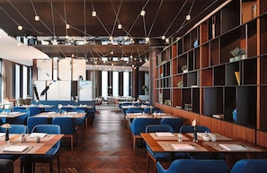 A restaurant with multiple tables and chairs, wooden floors, and a modern interior design. - Leonardo Royal Hotel Munich Bavaria Towers (Munich)