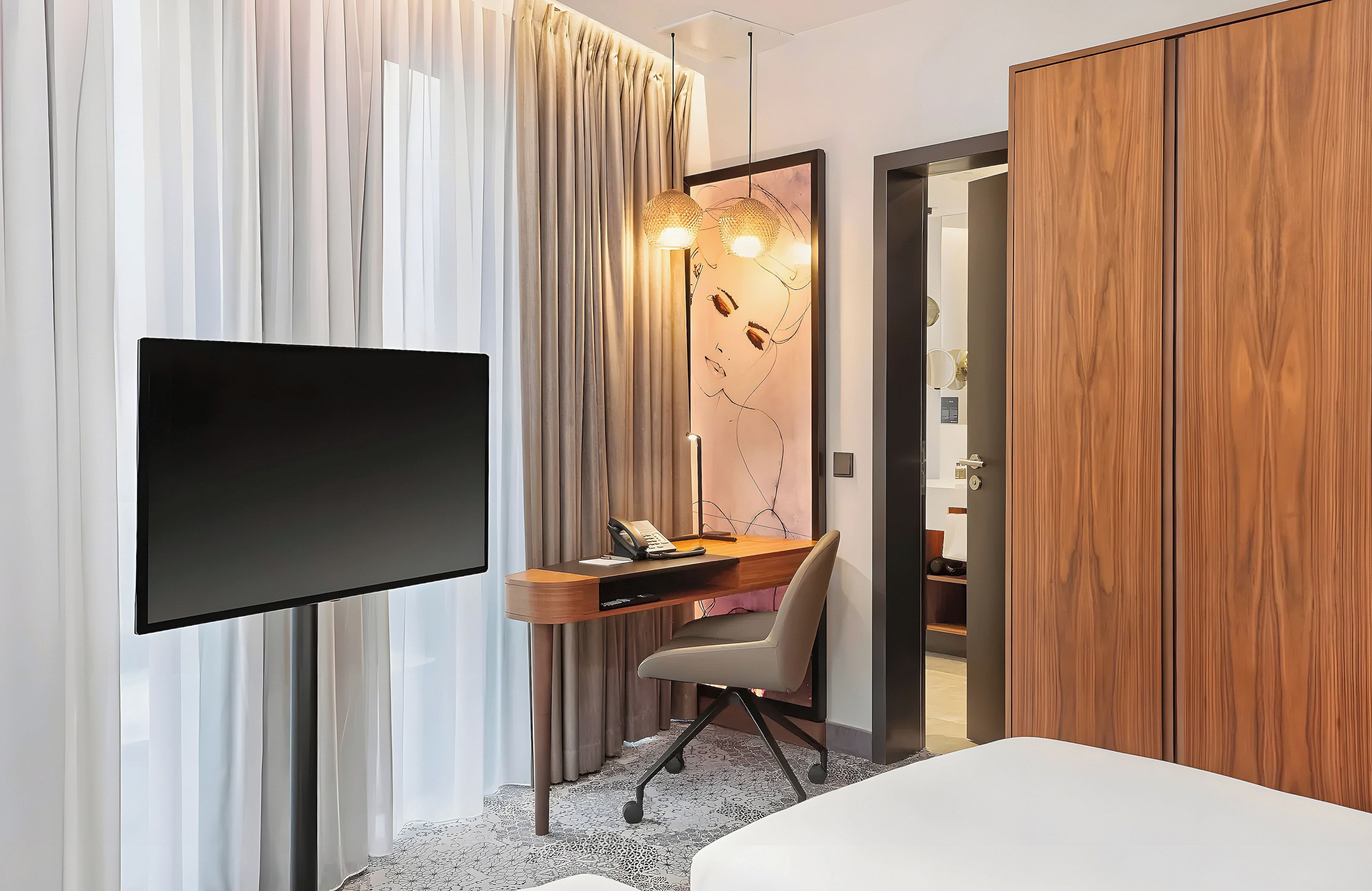 Una habitación de hotel con televisión de pantalla plana, un escritorio con silla, una cama y un armario.
