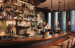A bar area with a variety of liquor bottles, a coffee machine, and seating. - Leonardo Royal Hotel Munich Bavaria Towers (Munich)