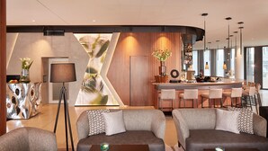 A modern hotel lobby with a bar area, seating arrangements, and a large abstract artwork on the wall. - HYPERION Hotel München (Munich)