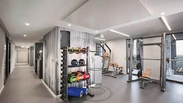Ein modernes Fitnessstudio mit Kraftgeräten, einer Hantelbank und einem an der Wand befestigten Gestell für Trainingsbälle.