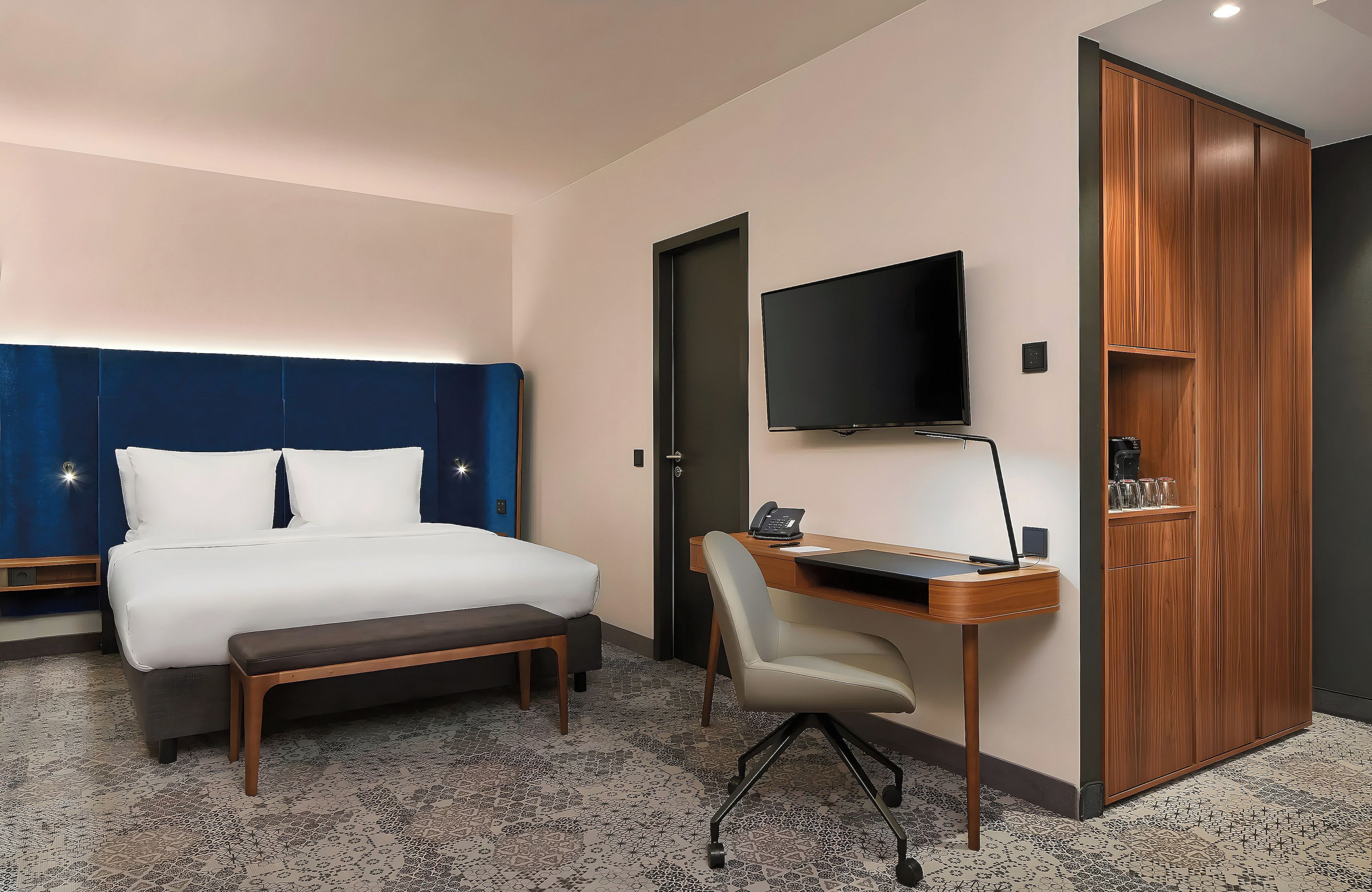 Habitación de hotel con cama, escritorio, silla, televisión y armario.