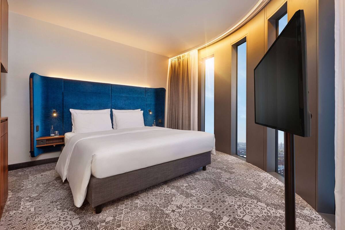 Una habitación de hotel moderna con una cama grande, un televisor de pantalla plana y vistas a la ciudad.