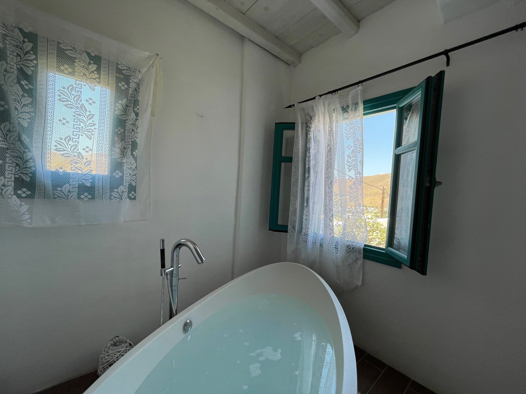 Un baño con una bañera independiente, un ventanal con contraventanas verdes y una ducha con un grifo moderno.