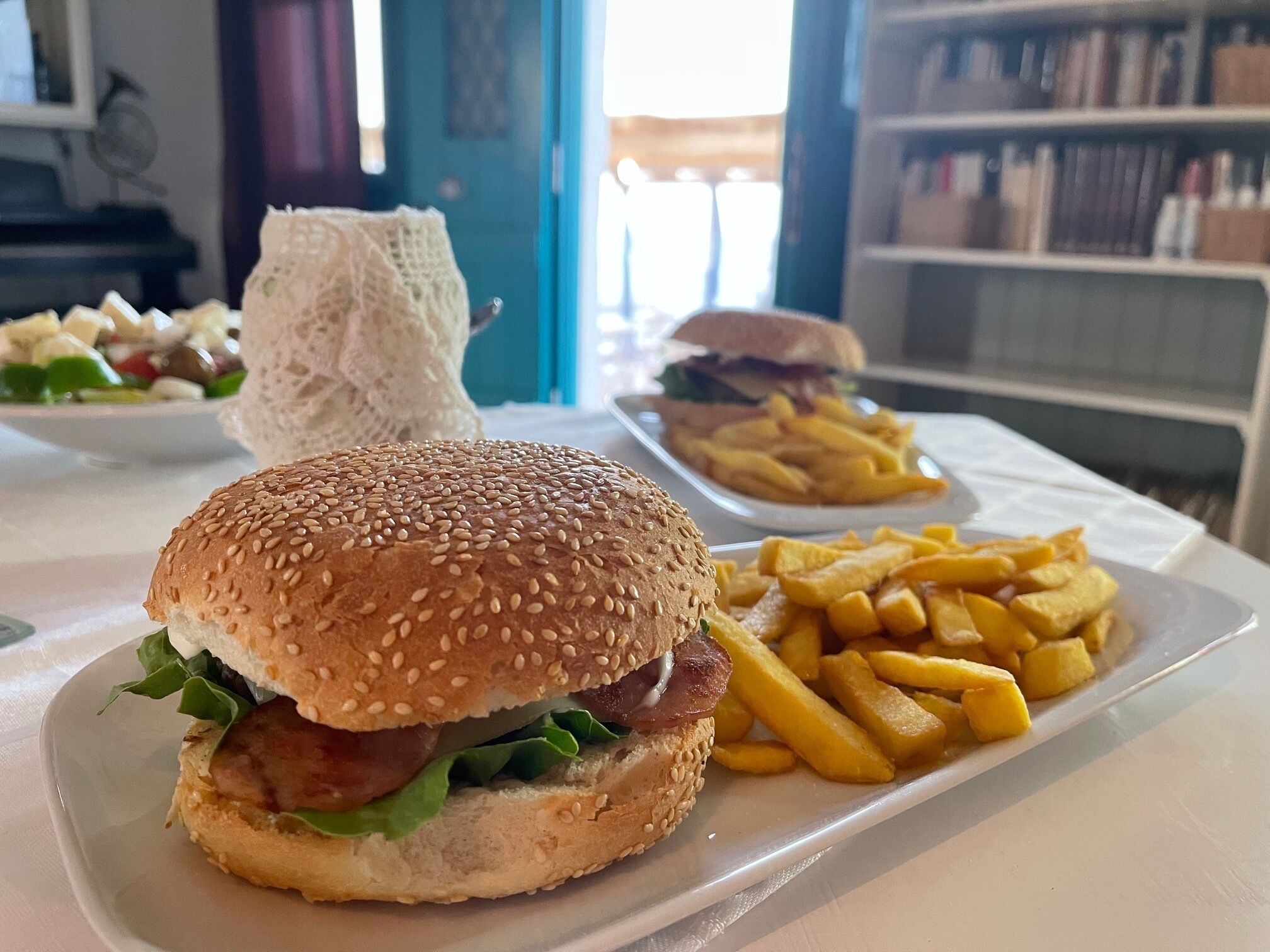 Una comida que incluye una hamburguesa, papas fritas y una ensalada sobre un mantel blanco.