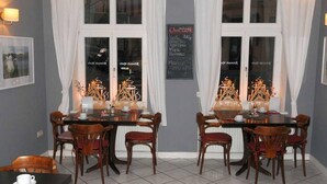 Un comedor con una mesa y sillas, un menú en una pizarra y vistas de la calle a través de las ventanas.