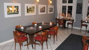 Comedor con una mesa larga, sillas con cojines rojos y cuadros en la pared.