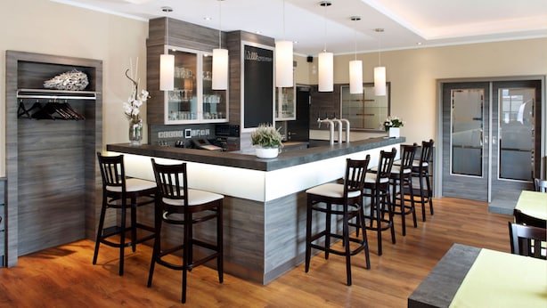 A modern kitchen with a large island, bar stools, pendant lights, and built-in appliances. - Hörster Krug (Lage)