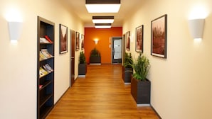 A hotel hallway with wooden flooring, framed pictures on the walls, and potted plants. - Hörster Krug (Lage)