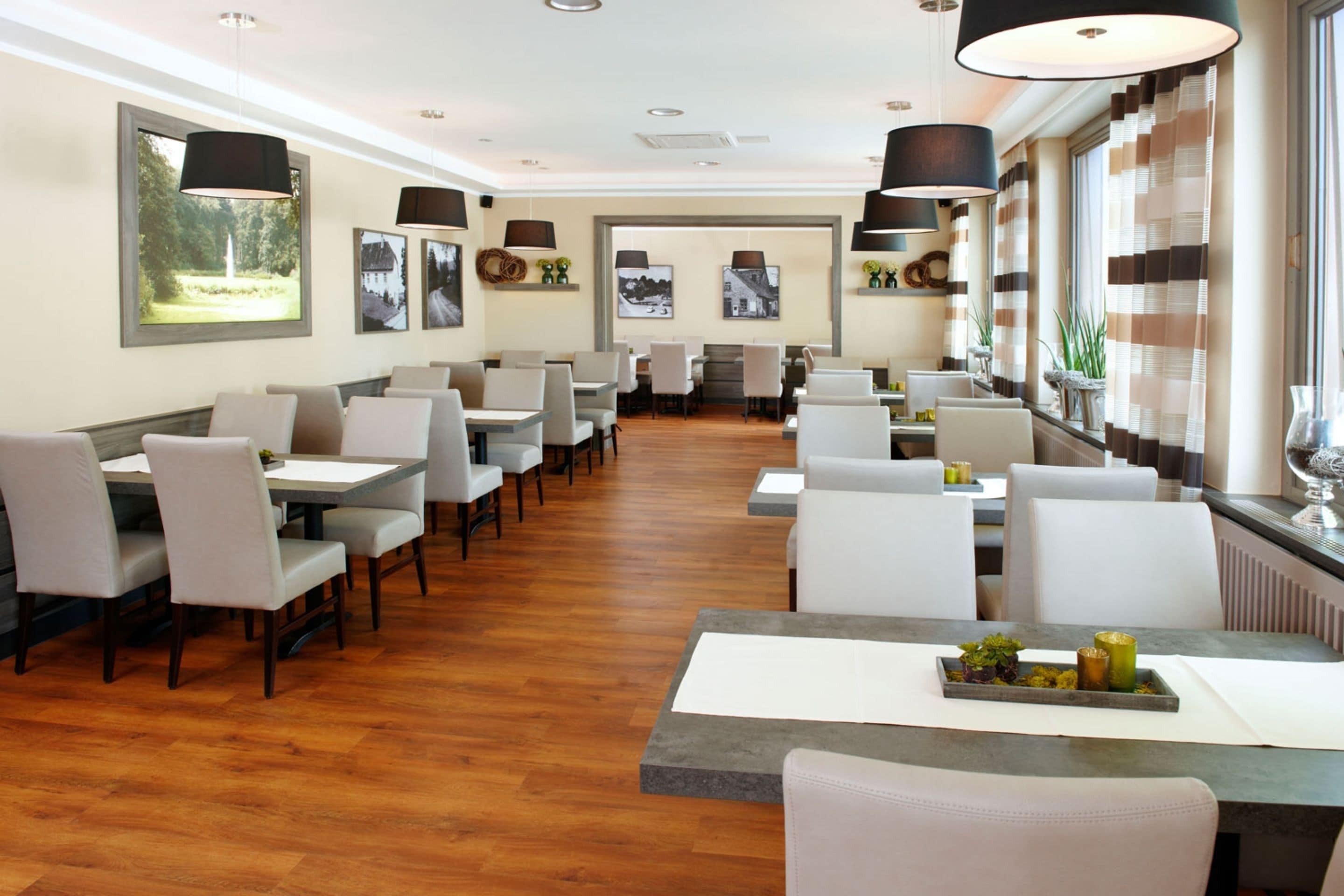 A restaurant with a long counter and multiple tables, wooden flooring, and pendant lighting.