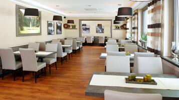 A restaurant with a long counter and multiple tables, wooden flooring, and pendant lighting.