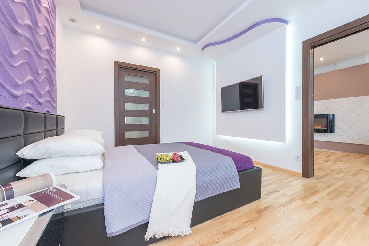 Un dormitorio moderno con una cama, un televisor montado en la pared y piso de madera.