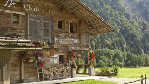 A wooden chalet hotel named "Chalet Hôtel les fermes de Pierre & Anna Accueil" with flower boxes and a stone wall. - Les Fermes de Pierre et Anna (Le Grand-Bornand)