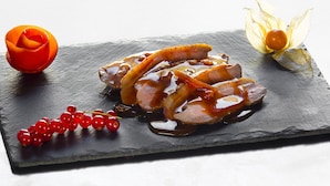 A black slate serving board with sliced meat and sauce, garnished with red currants and a flower. - Les Fermes de Pierre et Anna (Le Grand-Bornand)