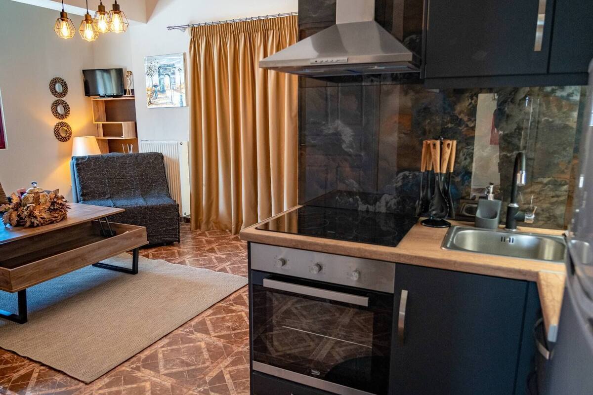A compact kitchen with a black stove, oven, and modern sink. There is a dining area with a wooden table and a sofa.