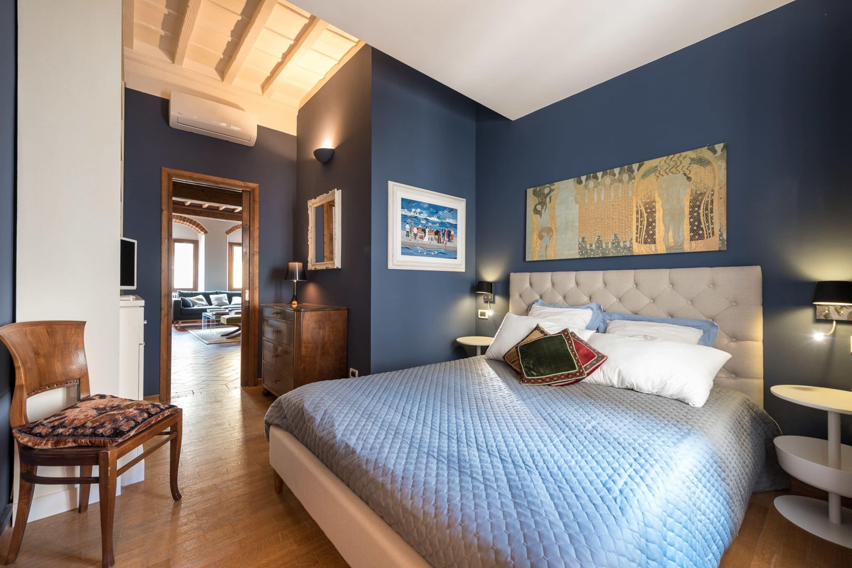 Een slaapkamer met een groot bed, een houten stoel, een nachtkastje en een nachttafel.