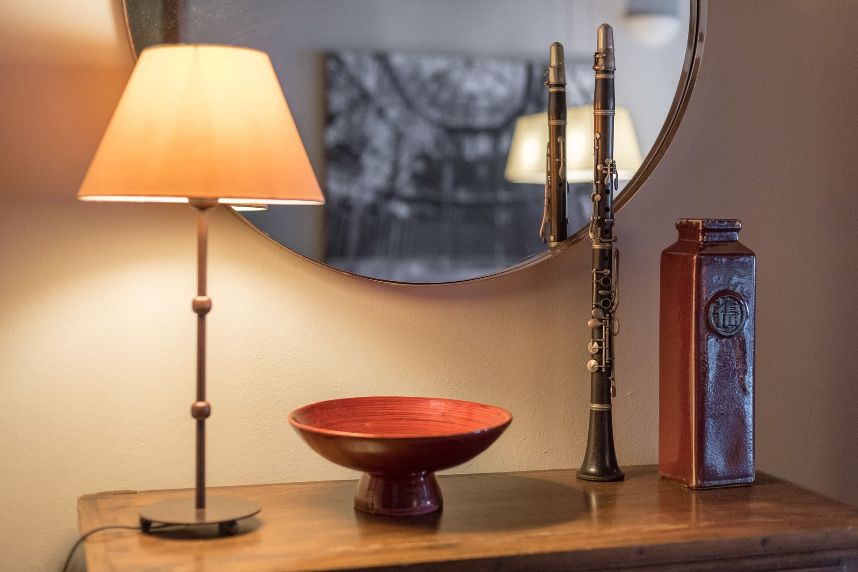 A wooden table with a red bowl, a lamp, a mirror, and a flute.