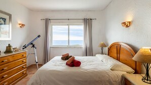 Ein ordentlich gemachtes Bett, zusammenge rollte Handtücher, eine Holzkommode, ein Teleskop und eine Lampe auf einem Nachttisch.