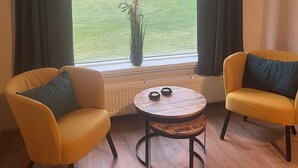 Una habitación con dos sillones amarillos, una mesita redonda y vistas a un campo verde a través de amplios ventanales con cortinas oscuras.