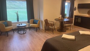 Una habitación de hotel con cama, dos sillones, una mesita, una mesa de comedor y una zona de cocina.