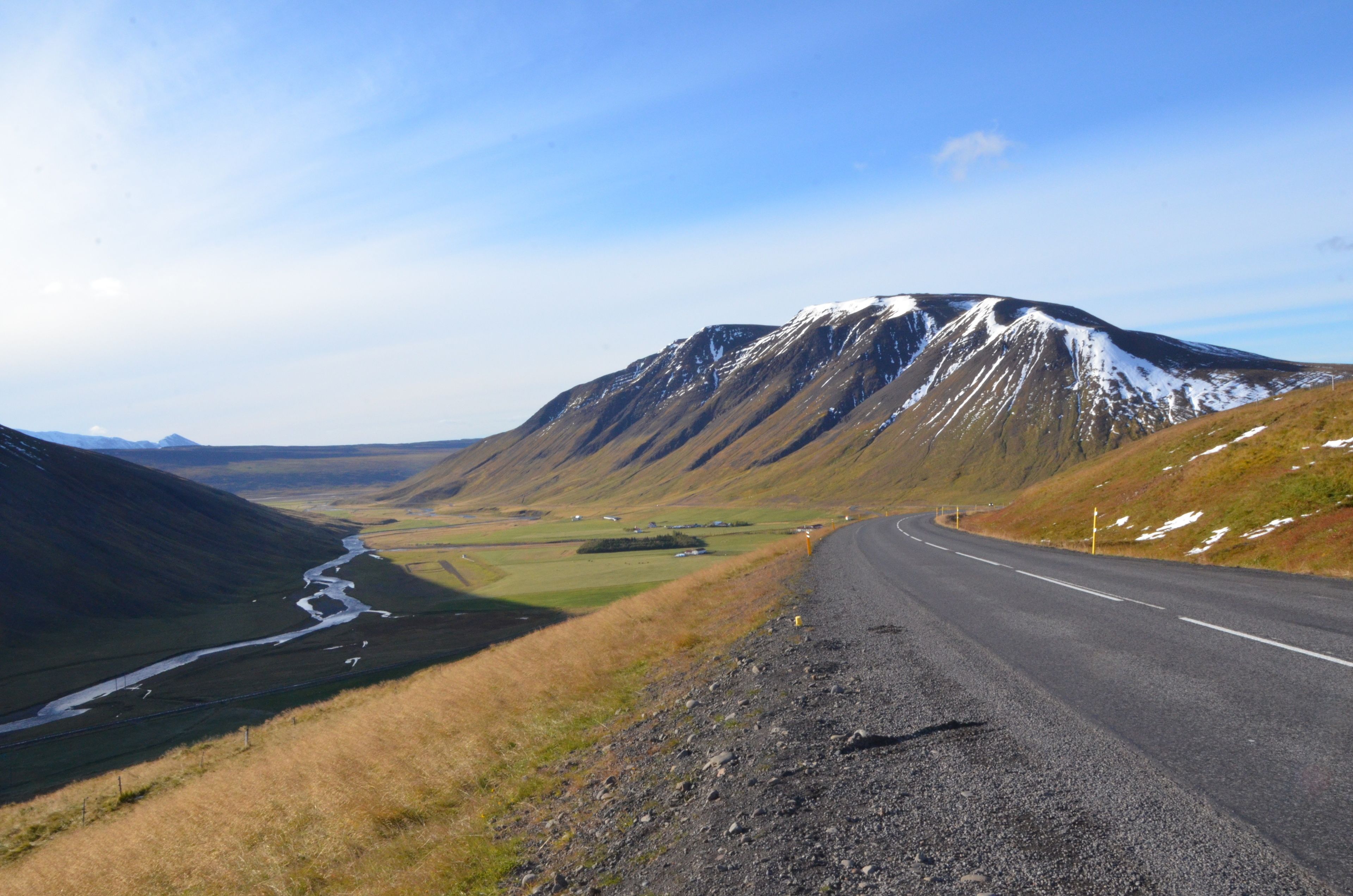 A winding road in a mountainous area with a river running parallel to the road.
