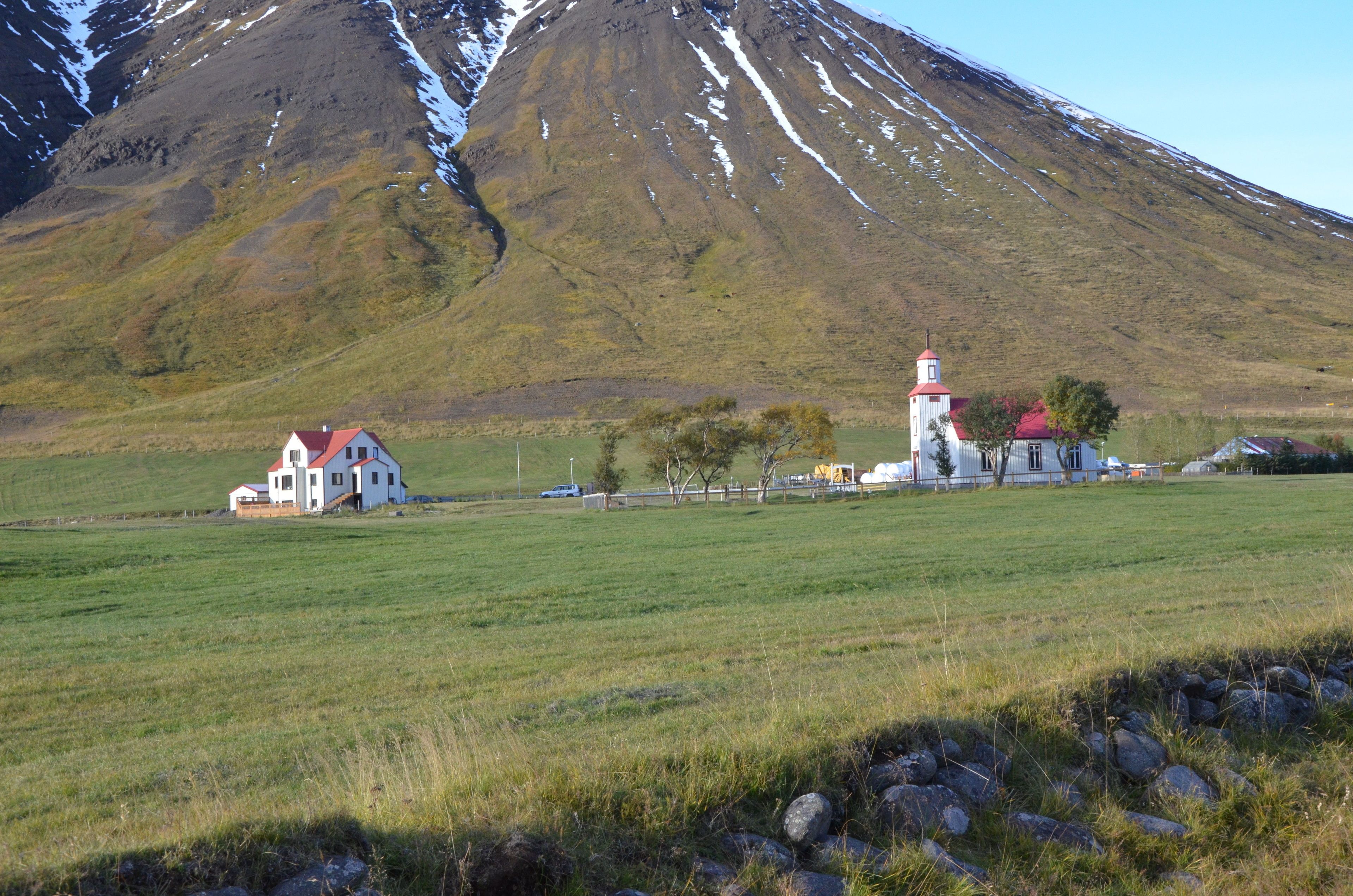 A rural landscape with a church, a white house, and a mountain in the background.