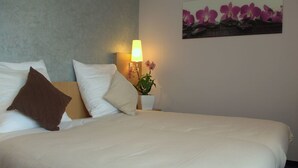 A neatly made bed with white and brown pillows, a bedside lamp, and a potted orchid on the nightstand. - Hotel Beuss (Oberursel)