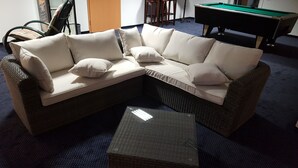 A corner sectional sofa with cushions, a small side table, and a pool table in the background. - Hotel Beuss (Oberursel)