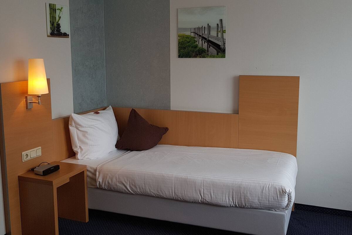 A hotel room with a bed, a nightstand with a lamp, and a wall-mounted TV.