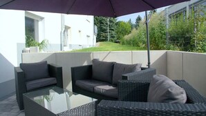 An outdoor patio area with wicker furniture, a glass table, and a purple umbrella. - Hotel Beuss (Oberursel)