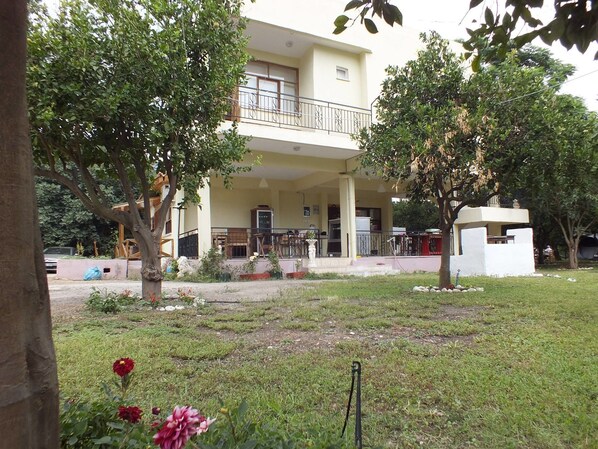 A building with a balcony, surrounded by trees and a grassy area.